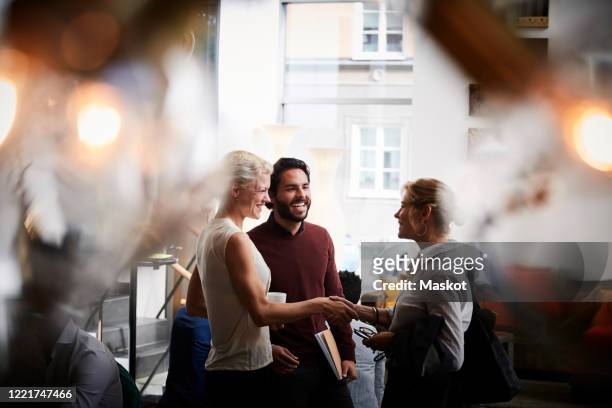smiling businesswoman shaking hands with female coworker while standing by colleague in seminar at workplace - representative member of congress stockfoto's en -beelden
