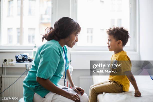 female pediatrician looking at mischief boy in clinic - naughty nurse images stock-fotos und bilder