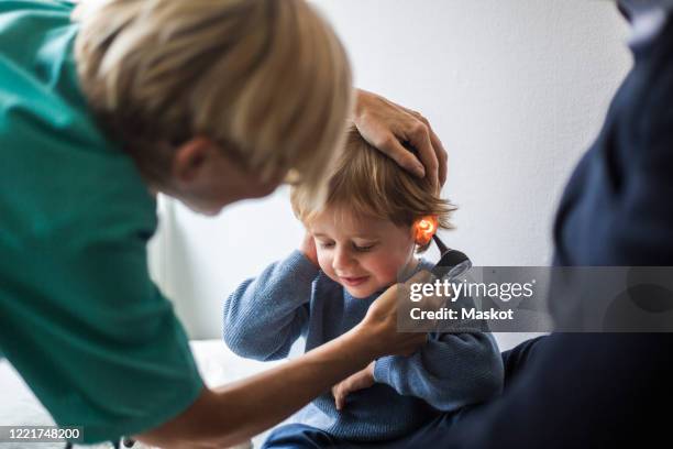 female doctor examining boy's ear with otoscope in hospital - doctor with child stockfoto's en -beelden
