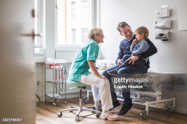 side view of smiling female doctor talking to boy with father in clinic - pediatric imagens e fotografias de stock