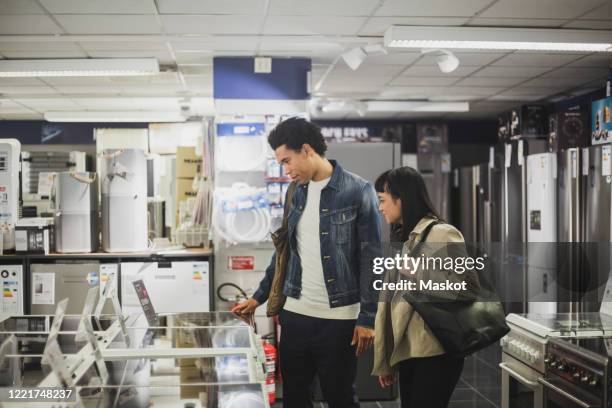 male and female friends looking at appliances in electronics store - buying appliances stock pictures, royalty-free photos & images