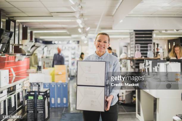 portrait of smiling mature female owner with boxes standing in electronics store - electronic stock-fotos und bilder