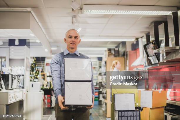 mature salesman with boxes walking in electronics store - appliance store stock pictures, royalty-free photos & images