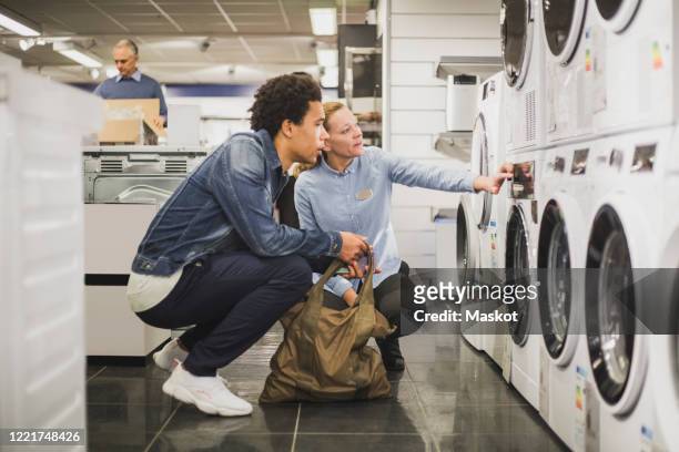 mature owner explaining about washing machine to customer in electronics store - equipo eléctrico fotografías e imágenes de stock