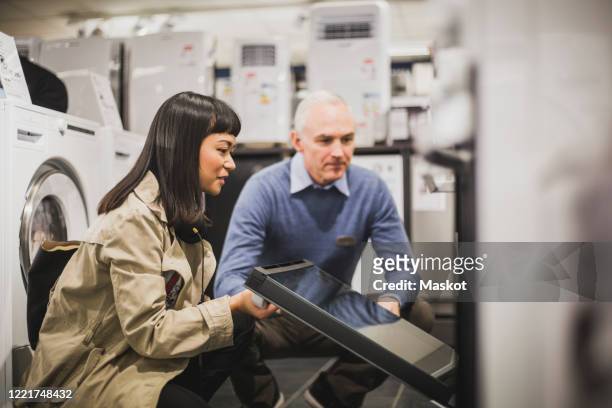 female customer looking at oven while crouching by owner in electronics store - electrical shop stock pictures, royalty-free photos & images