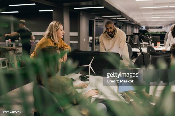 male and female coworkers discussing at office desk - kantoor milieus stockfoto's en -beelden