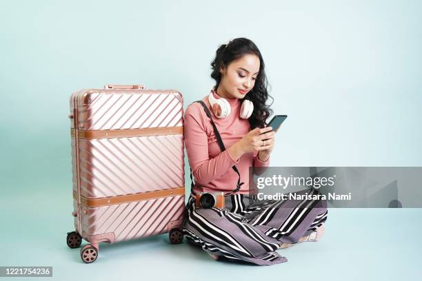 portrait of happy asian passenger travel tourist girl using mobile app to book the online seat of flight or check-in and sitting beside the suitcase. vacation destination. tourism concept. - airport advertising stock-fotos und bilder
