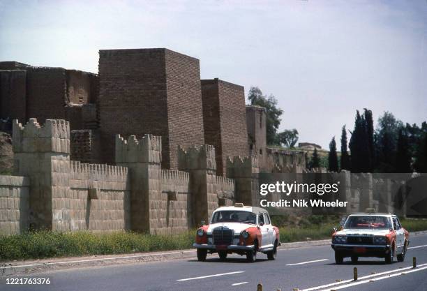 Taxis drive along road beside restored walls of ancient Akkadian and net-assyrian city pf Nineveh which from 662-612 BC was the largest city in the...