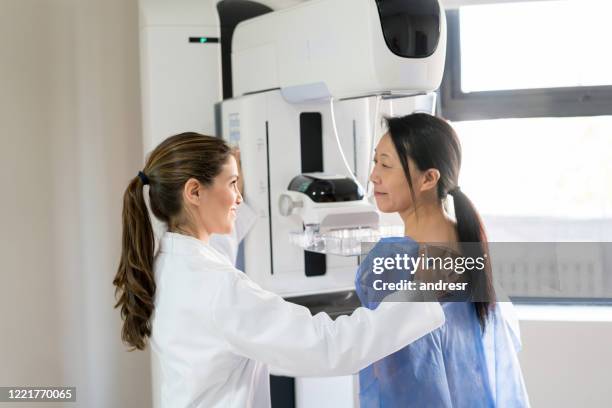 médico femenino hablando con su paciente y ajustando su posición para hacer una mamografía - seno fotografías e imágenes de stock