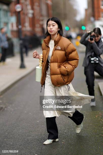 Guest wears a brown North Face puffer winter coat, a cream-color flowing dress, a white bag with a beaded pearl handle, black pants, white leather...