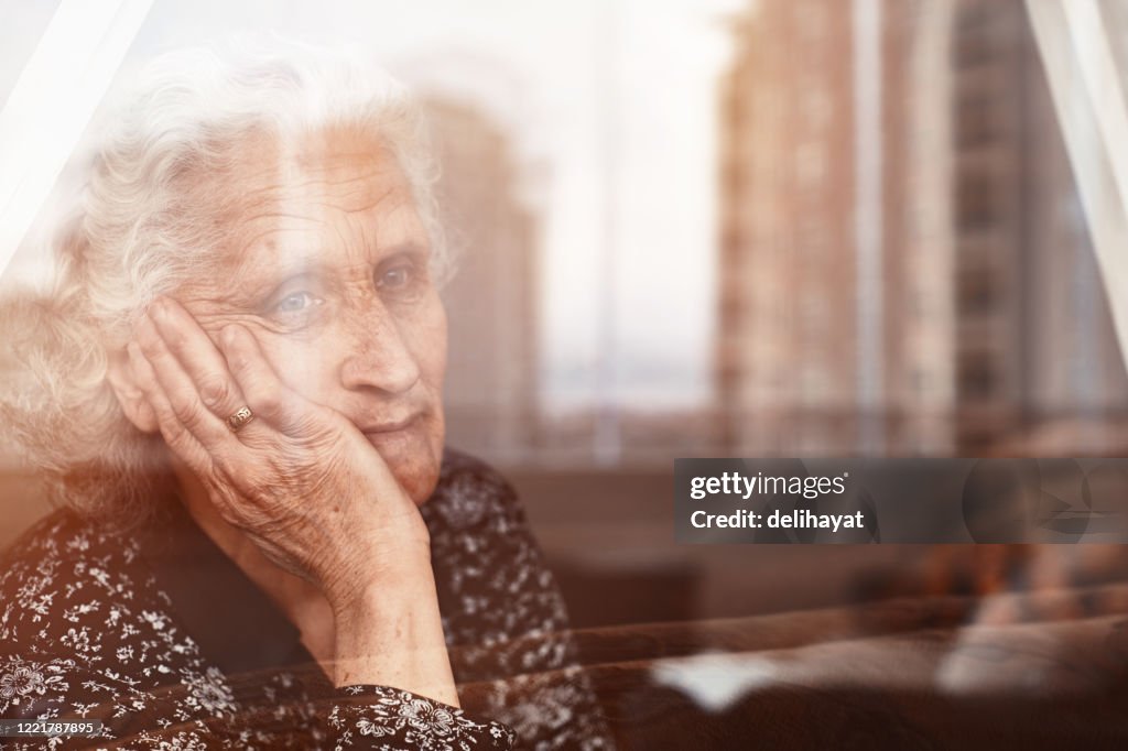 Mujer anciana sentada sola y mirando tristemente fuera de la ventana