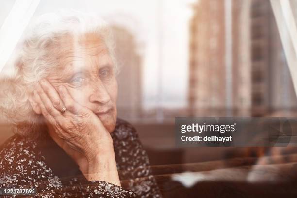 donna anziana seduta da sola e guardando tristemente fuori dalla finestra - solitario foto e immagini stock