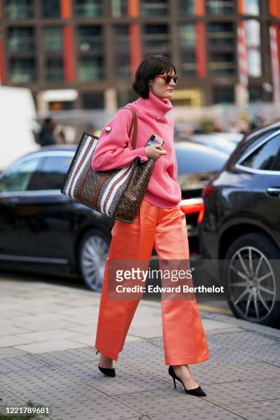 Guest wears sunglasses, a neon pink wool turtleneck pullover, a Burberry large monogram bag, neon orange shiny lustrous silky flare pants, black...