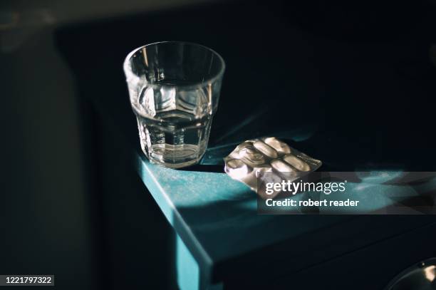 glass of water and medication pills blister pack on bedside table - slaappil stockfoto's en -beelden
