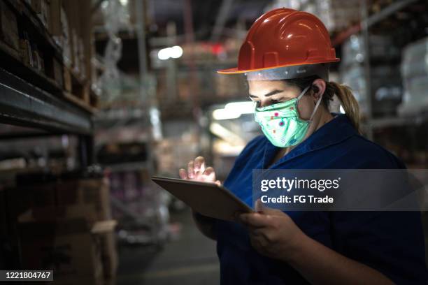 portrait of mid adult woman wearing face mask using digital tablet - working at warehouse / industry - serviços essenciais imagens e fotografias de stock