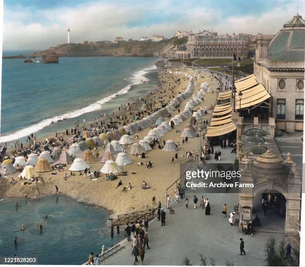 Colorize, elevated view of a crowded beach, full of bathers and cabanas, Biarritz, France, 1927. Visible in the background is the Hotel du Palais,...