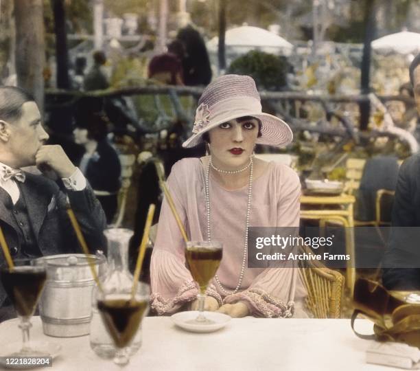 Colorized photo of Polish-born American actress Pola Negri seated at sidewalk table at the Cafe de la Paix, Paris, France, 1927.