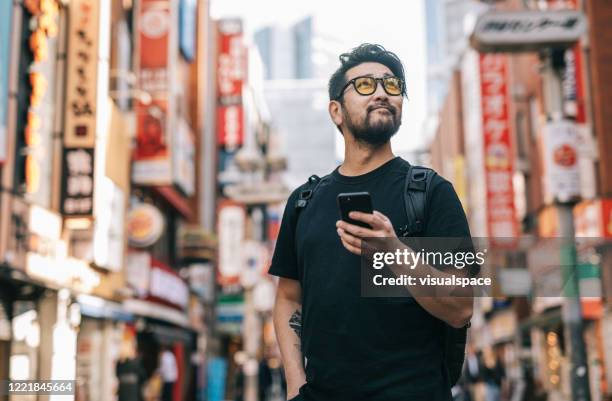 asiatischer mann erkundet die stadt und hält ein smartphone in der hand - erforschung stock-fotos und bilder
