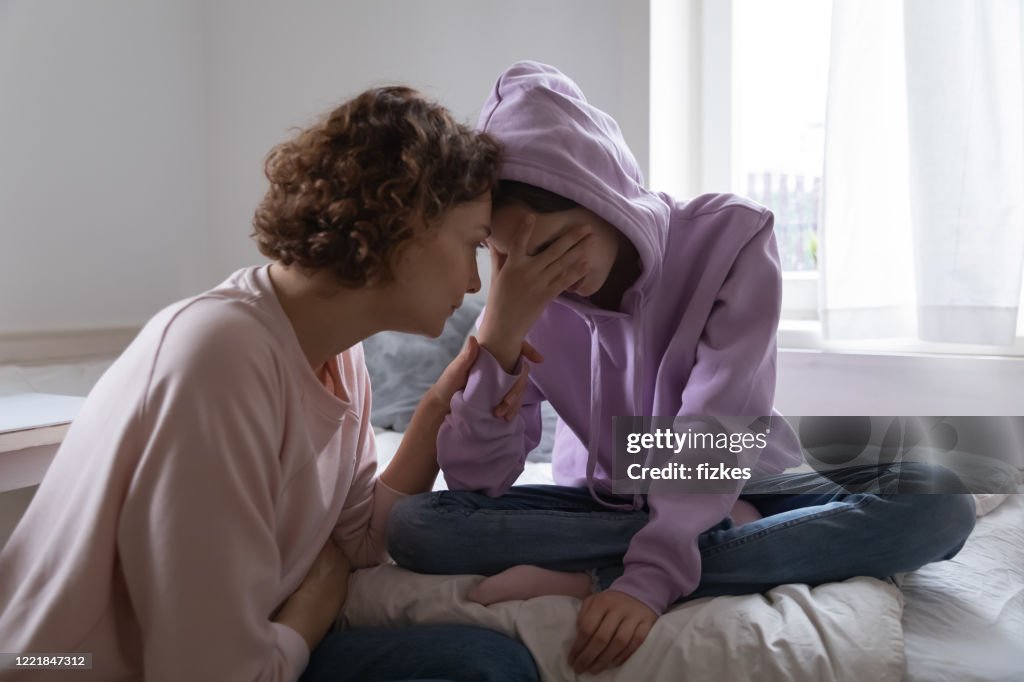 Worried mom comforting depressed teen daughter crying at home