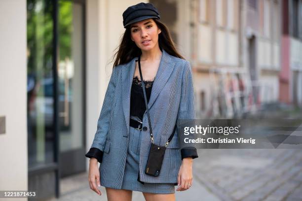 Dora Molina is seen wearing grey checkered blazer and mini skirt, black Lazzo phone case, boy baker hat on April 29, 2020 in Berlin, Germany.