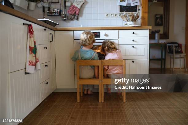 rear view of two small children looking at pizza in oven at home, waiting. - waiting stock pictures, royalty-free photos & images