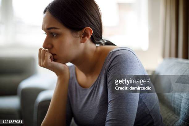 upset woman sitting on sofa alone at home - guilt stock pictures, royalty-free photos & images