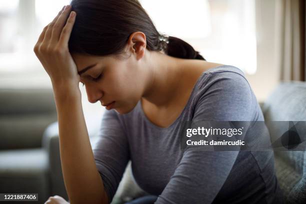 verärgerte frau sitzt allein zu hause auf dem sofa - chronic fatigue stock-fotos und bilder