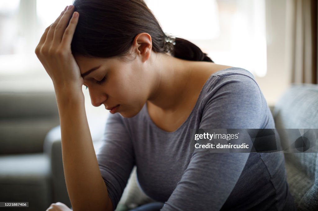 Upset woman sitting on sofa alone at home