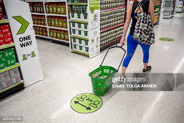 Shopper pulls a shopping basket past a floor sticker advising customers to maintain the British government's current social distancing guidelines and...