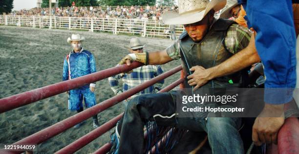 een latino bull rider het dragen van een beschermende veiligheidsvest zit op de top van een stier in een pen voordat concurreren in een bull riding event - bull riding stockfoto's en -beelden