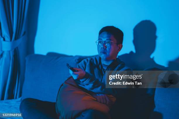 un asiatico cinese mid adulto guardando film a casa da solo di notte nel buio - man watching tv foto e immagini stock