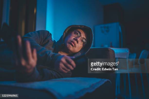 an asian chinese mid adult watching tv at home alone at night in darkness leaning on sofa - only mid adult men stock pictures, royalty-free photos & images