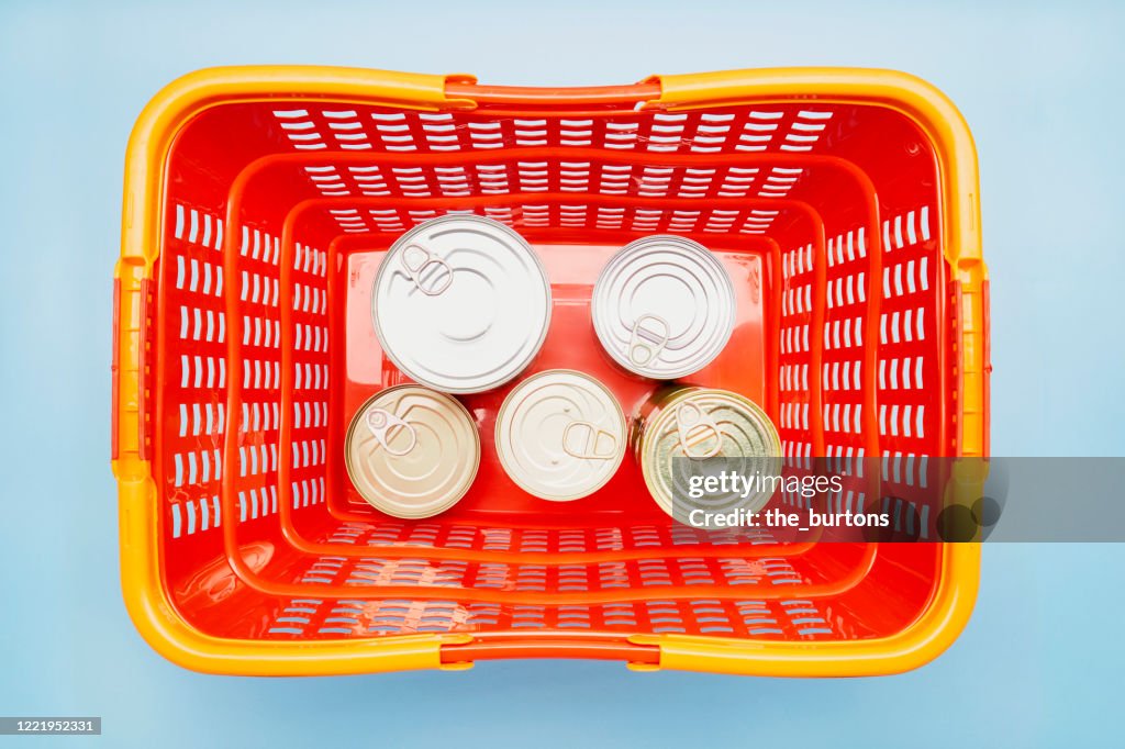 Still life of canned food in red shopping basket on blue background