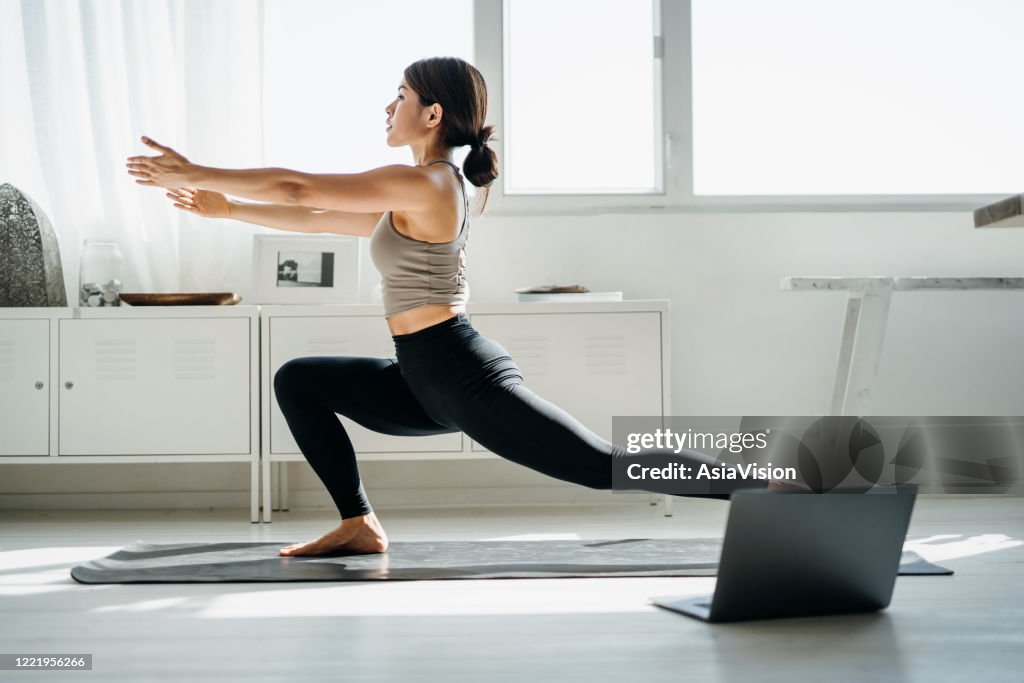 Joven asiática haciendo clase de yoga en línea con computadora portátil en la sala de estar en casa por la mañana