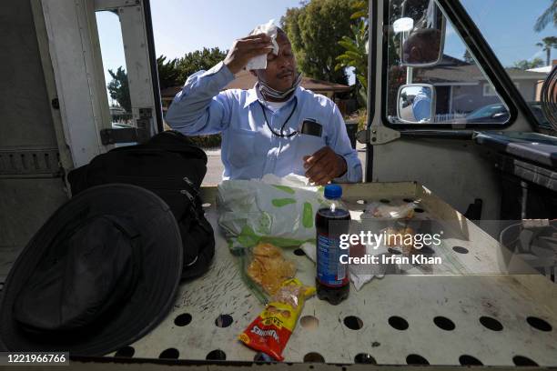 James Daniels wipes sweat from his forehead as he takes a break after a grueling walk in hot sun delivering mail on Friday, May 15, 2020 in San...