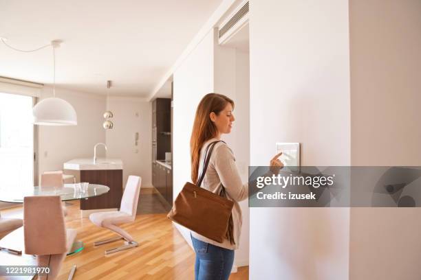 mujer activando el sistema de seguridad inteligente para el hogar antes de irse - thermostat fotografías e imágenes de stock