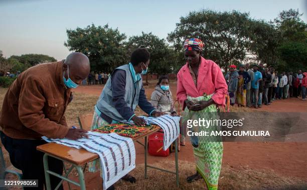 Electoral officials check the voters roll while people queue to vote at the Malembo polling station during the presidential elections in Lilongwe on...