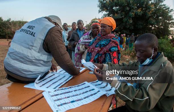 Electoral officials check the voters roll while people queue to vote at the Malembo polling station during the presidential elections in Lilongwe on...