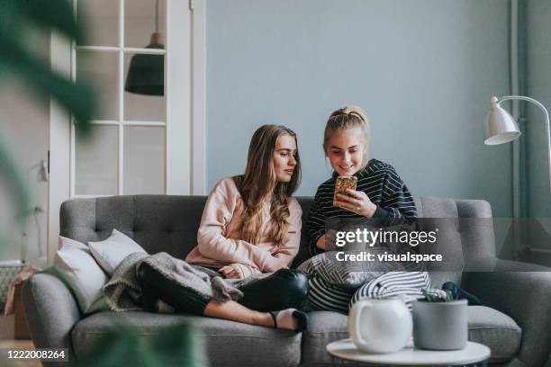 zwei teenager-mädchen mit smartphone zu hause auf der couch - tea for two stock-fotos und bilder