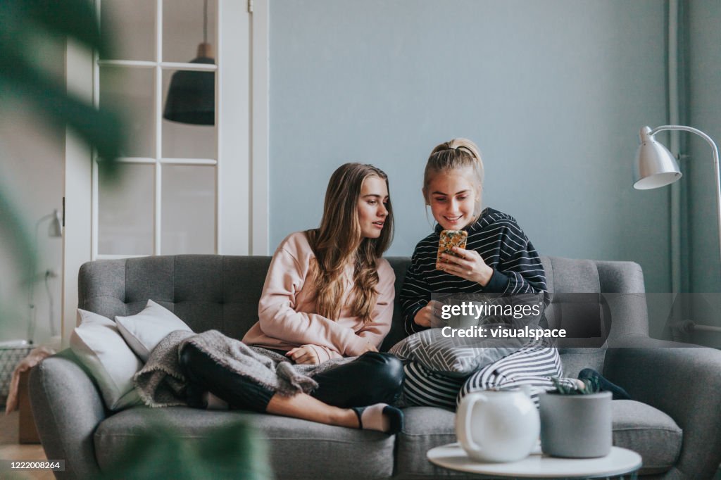 Twee tienermeisjes die slimme telefoon thuis op de laag gebruiken