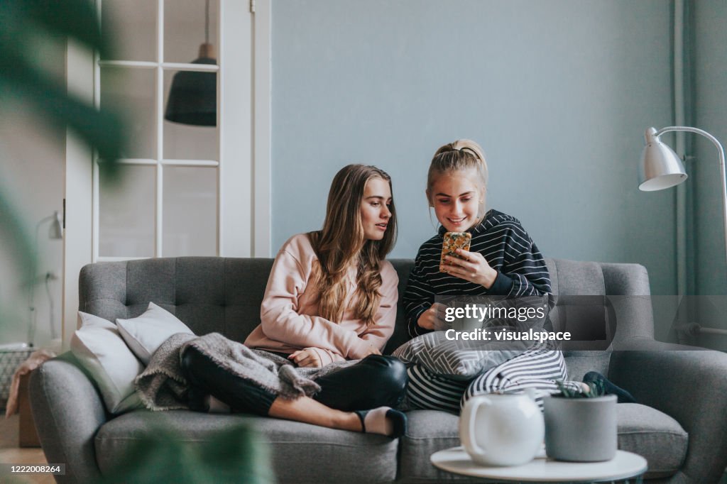 Two teenage girls using smart phone at home on the couch