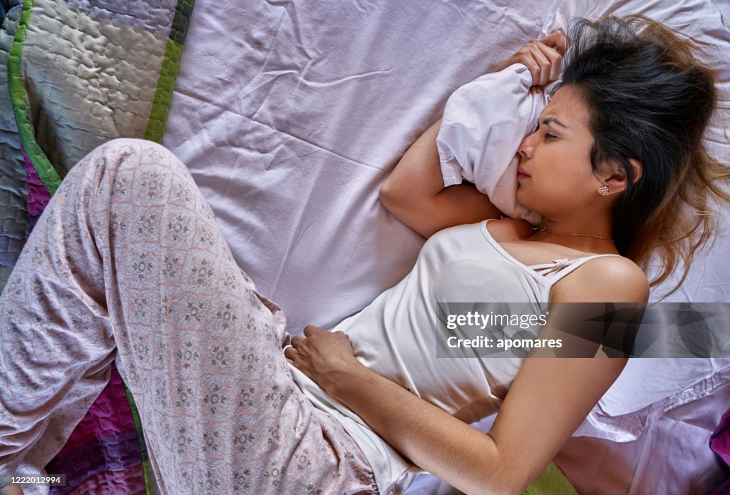 Hispanic young woman suffering PMS pain in bed