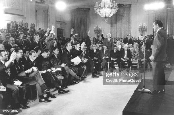 View of President Richard M. Nixon standing at a podium addressing questions from reporters during his first press conference in the East Room of the...
