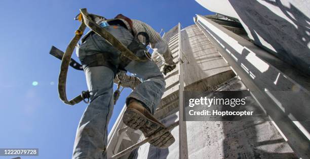 ein ölfeldarbeiter erklimmt an einem sonnigen morgen eine leiter an der seite eines schlammtanks auf einer öl- und gasbohranlage - arbeitsstiefel stock-fotos und bilder