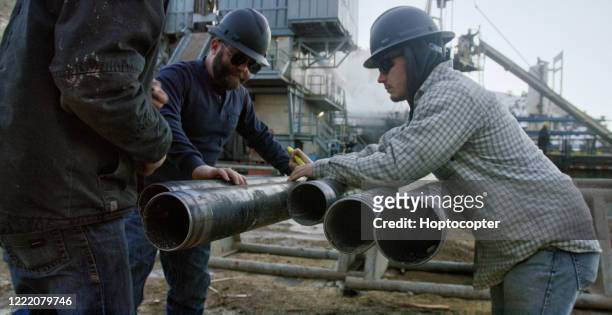 three oilfield workers remove the drilling pipe thread protector caps at an oil and gas drilling pad site on a sunny day - oil and gas workers imagens e fotografias de stock