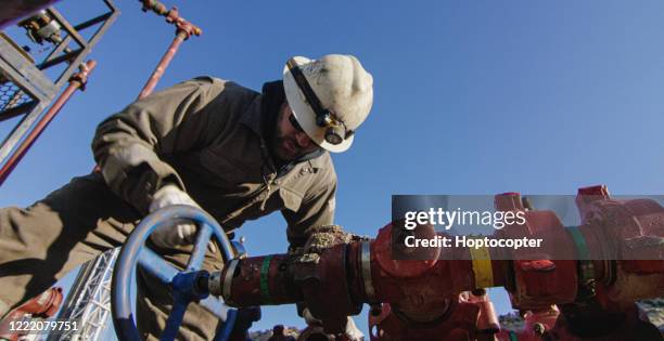 een arbeider van het olieveld in zijn jaren '30 pompt onderaan lijnen bij een plaats van het boorpad van de olie en van het gas op een koude, zonnige, de ochtend van de winter - pipeline stockfoto's en -beelden