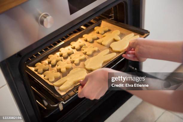 teenager putting a tray of shaped raw cookies into a hot over for baking - girls hands behind back stock-fotos und bilder