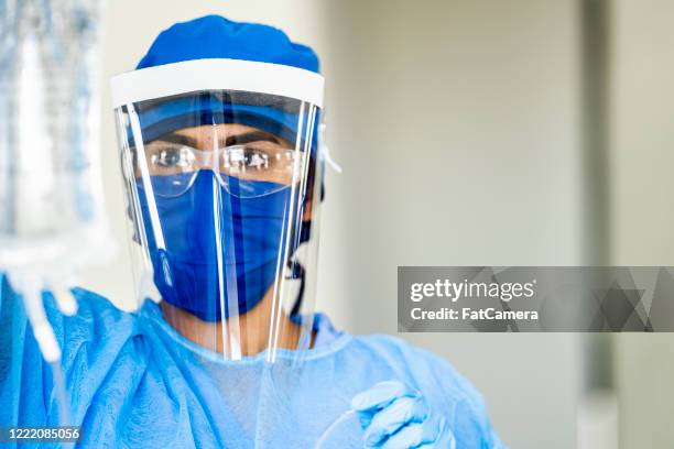 female middle eastern doctor hanging iv drip while wearing protective medical equipment - social distancing hospital stock pictures, royalty-free photos & images