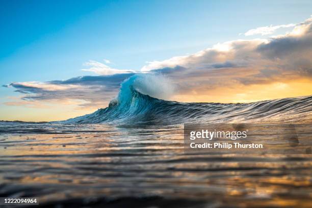 colorida ola alcanzando un pico en una llamarada con tormenta al amanecer - imponente fotografías e imágenes de stock