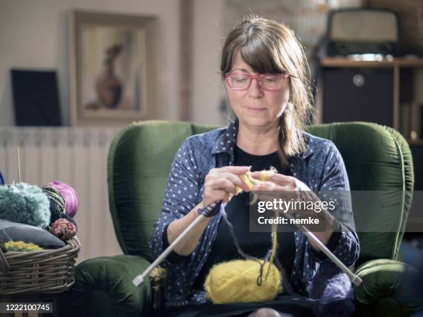 home hobbie, donna di mezza età seduta e a maglia a casa - lavorare a maglia foto e immagini stock